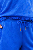 Close-up of the royal blue embossed tropical leaf fabric, fringe top hem and adjustable drawstring waist with gold-tone tips.