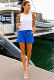 Woman wearing Royal Leaf Textured Shorts with a white boxy tank, clear platform sandals and coffee at a marina.