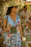 Woman wearing a colorful smocked patchwork print midi dress with a deep V-neckline, green sun hat, woven handbag, green sunglasses, and croc leather flip flops at an elegant summer garden party. Felicite Clothing Smocked Dress style 3911-41890 in french blue.