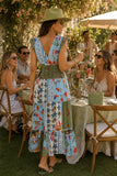 Woman wearing a colorful smocked patchwork print midi dress with a deep V-neckline, green sun hat, woven handbag, green sunglasses, and croc leather flip flops at an elegant summer garden party. Felicite Clothing Smocked Dress style 3911-41890 in french blue.