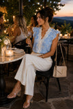 Woman in a stylish outfit sitting outdoors at sunset, holding a glass of wine.