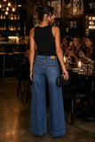 Rails Clothing Dover Palazzo Denim Pant Style 730A-255D-8419 in Boondocks. Woman wearing the Dover Wide Leg Palazzo Jeans with a black ribbed tank top, black strappy heels and a woven blck clutch at an upscale restaurant. Mid-rise drapey denim palazzo jeans with an adjustable tie waist styled for an edgy date night or dinner with friends.