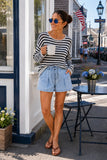Woman at a beach town coffee shop wearing the Evangeline ivory and dark navy striped open-weave linen blend sweater with pleated denim shorts for a daytime look. Rails Evangeline Sweater Style 826D-350D-8756 in Ivory Indigo Stripe.