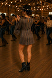 Back view of the Drifter Mini Dress showing the keyhole back detail while line dancing in a rustic barn with black western ankle boots and a black embellished hat.