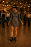 Woman wearing the Drifter Mini Dress with black western ankle boots and a black embellished rancher hat while line dancing in a rustic Hudson Valley barn.