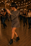 Woman in the Drifter Mini Dress performing a country line dance in a rustic barn wearing black western ankle boots, turquoise jewelry, and a black rancher hat.