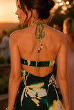 Woman wearing a tropical print beaded halter maxi dress with an open back, styled for a luxury resort vacation, beach dinner, destination wedding, or summer evening event. Steve Madden Apparel Strada Dress Style XB14040 in Golden Palm.