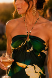 Woman wearing a tropical print beaded halter maxi dress with an open back, styled for a luxury resort vacation, beach dinner, destination wedding, or summer evening event. Steve Madden Apparel Strada Dress Style XB14040 in Golden Palm.
