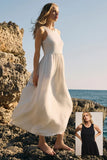 Woman in a white dress standing on rocky terrain by the ocean, with a smaller inset of her in a black dress.